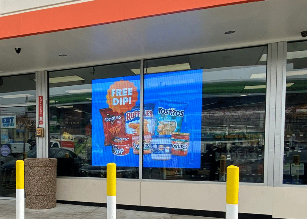 Transparent Digital Mesh hanging in a storefront window of a convenience store.