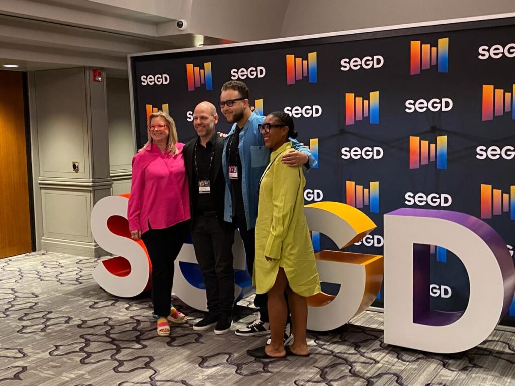 Attendees taking photos at the SEGD conference display featuring oversized branded letters and backdrop.