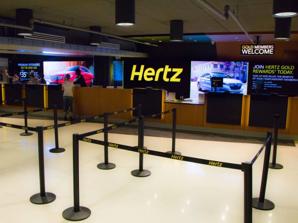 Hertz airport rental counter with digital displays, branded environmental graphics, and queue management signage by Gable.