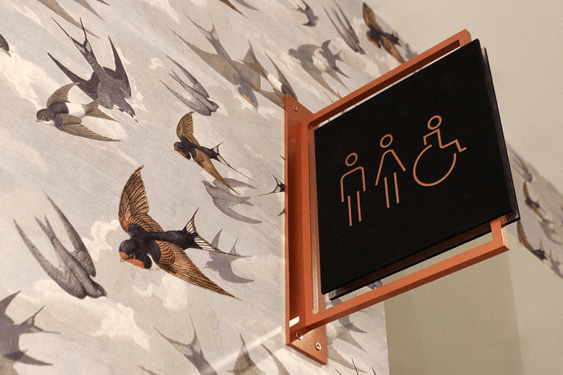 Restroom wayfinding sign with accessibility icons and decorative environmental graphics by Gable.