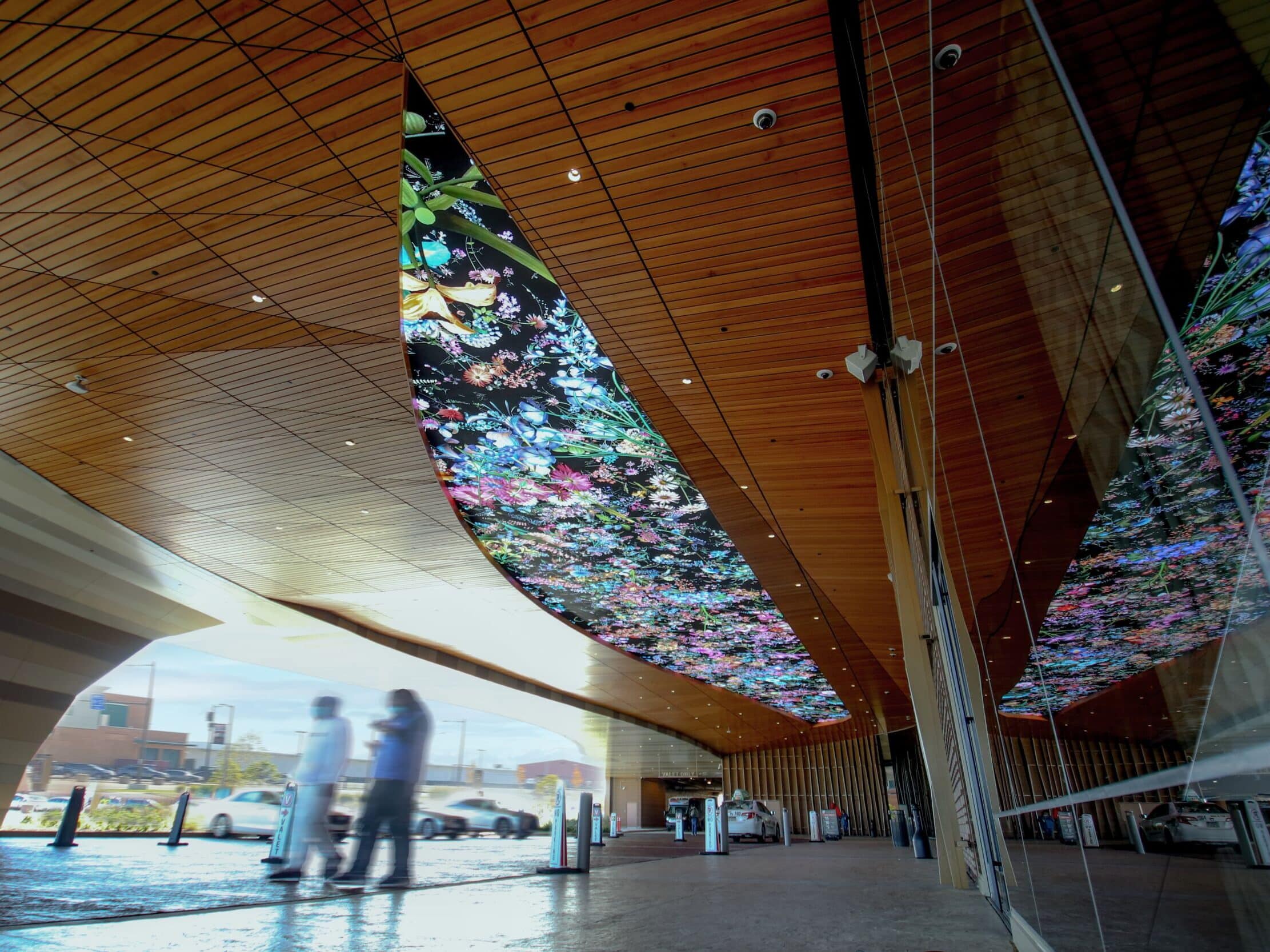 Reflective glass facade and digital canopy artwork at a contemporary hospitality entrance.
