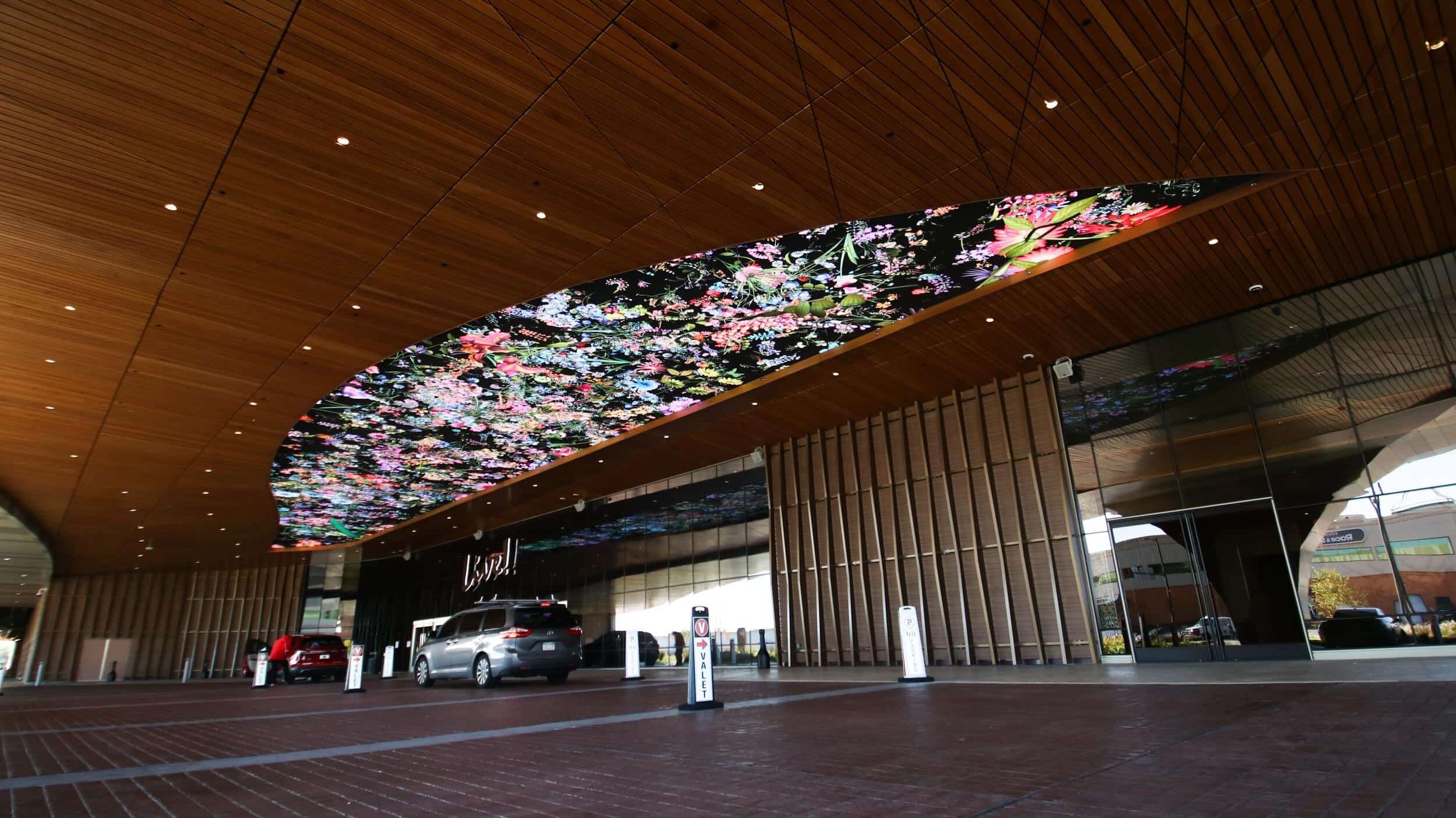 Resort porte cochere with large curved digital ceiling display and valet drive at the main entrance.
