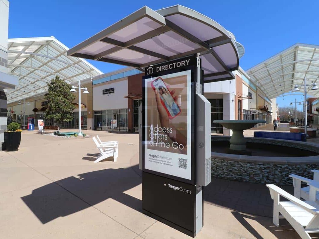 Outdoor shopping center digital directory kiosk beneath a canopy in an open-air retail plaza.
